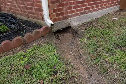 Downspout ending at the edge of a concrete slab with the soil washed out beneath it
