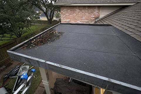 Low-slope section behind a patio cover, dark rolled surface with a seam running across it