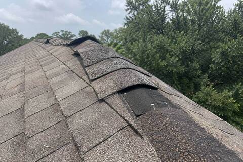 Lifted shingles along a roof ridge with nail heads exposed