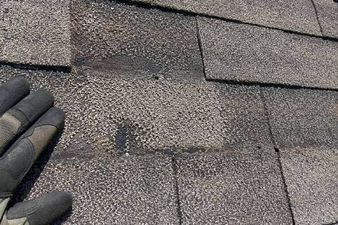 Close-up of a shingle surface with the granules worn thin and the mat showing through