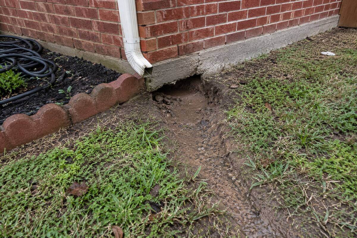 Downspout ending at the edge of a concrete slab with the soil washed out beneath it