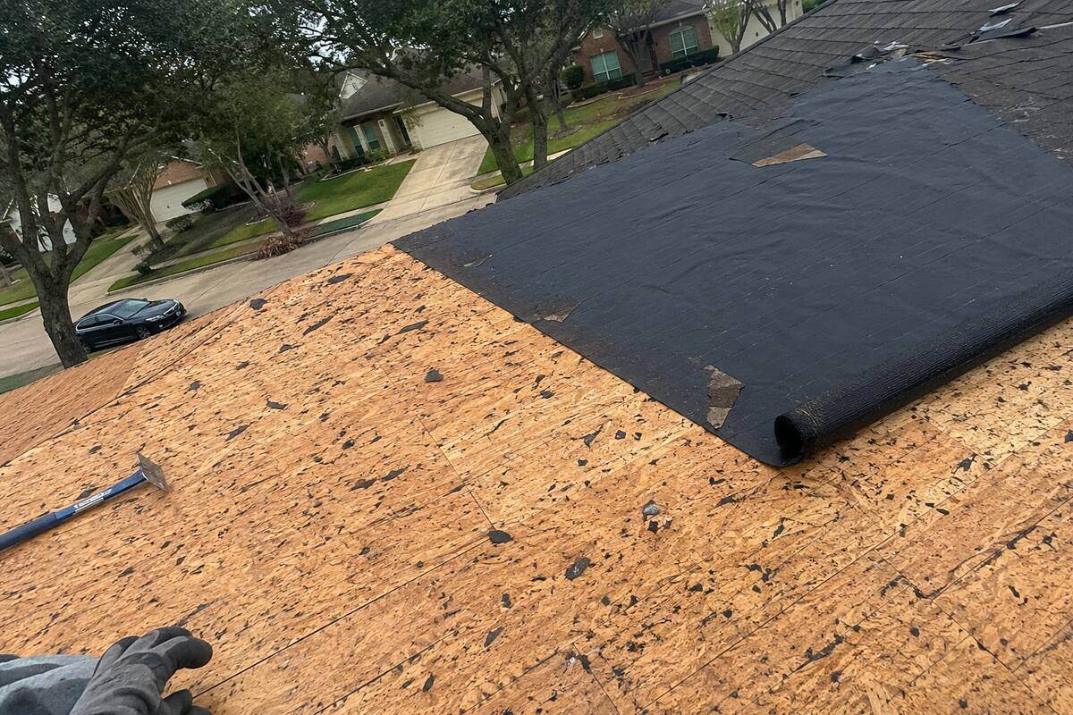Roof section stripped down to bare wood decking with underlayment partly rolled out
